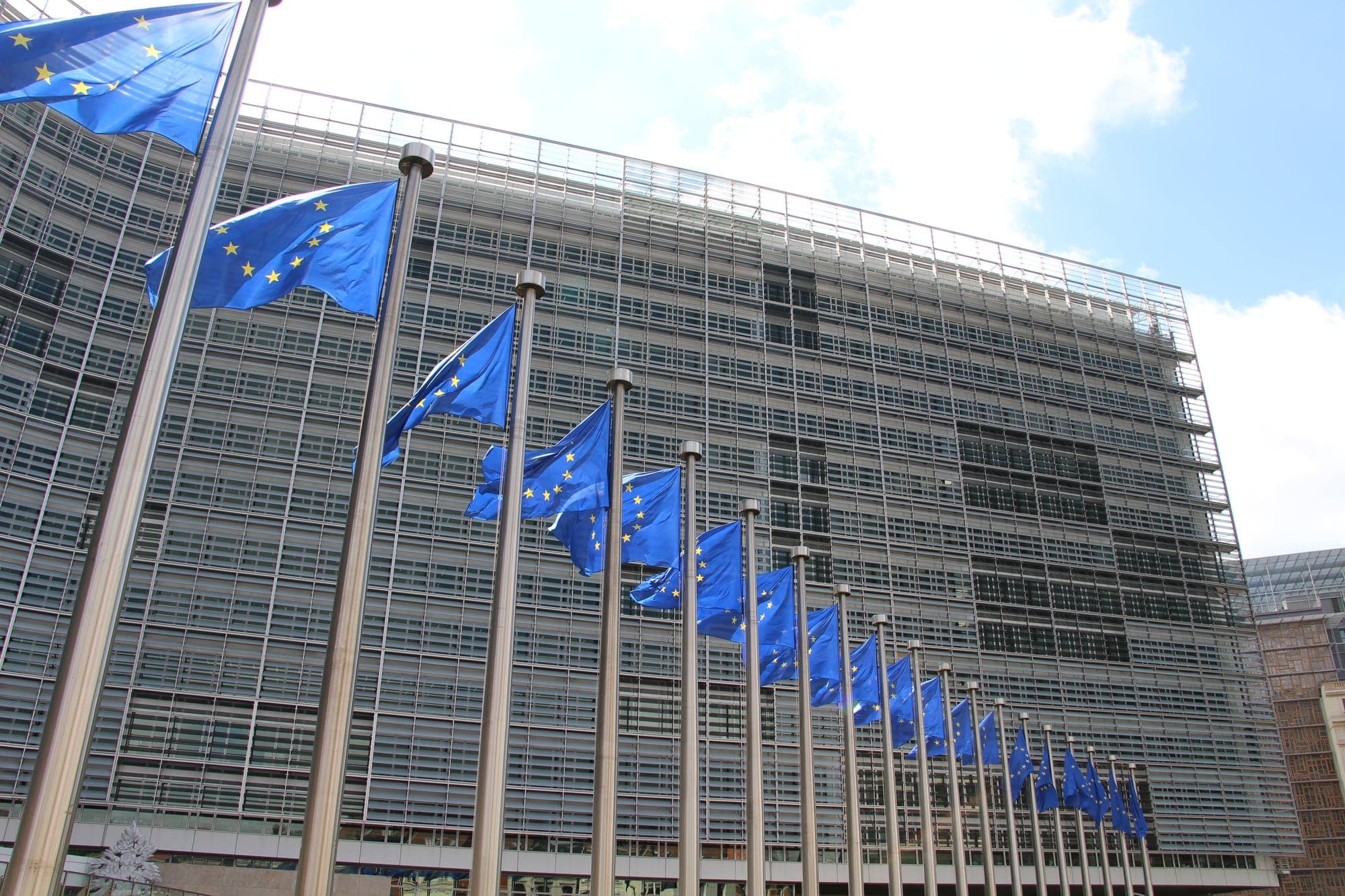 Drapeaux européens alignés sur leurs mâts devant la façade vitrée du Berlaymont, siège de la Commission européenne à Bruxelles