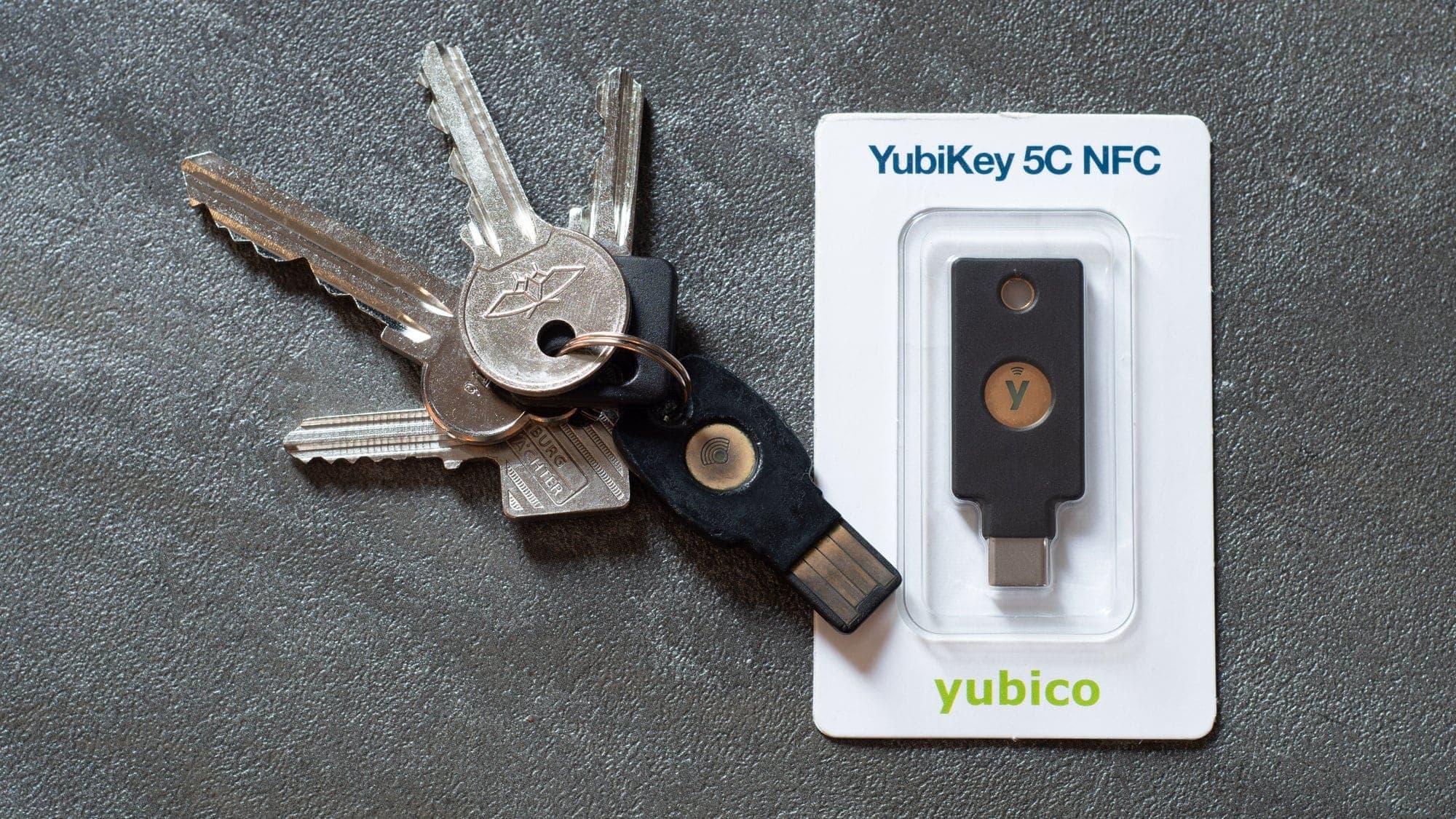 Une clé de sécurité YubiKey 5C NFC dans son emballage, posée à côté d'un trousseau de clés de maison auquel est accrochée une clé de sécurité USB