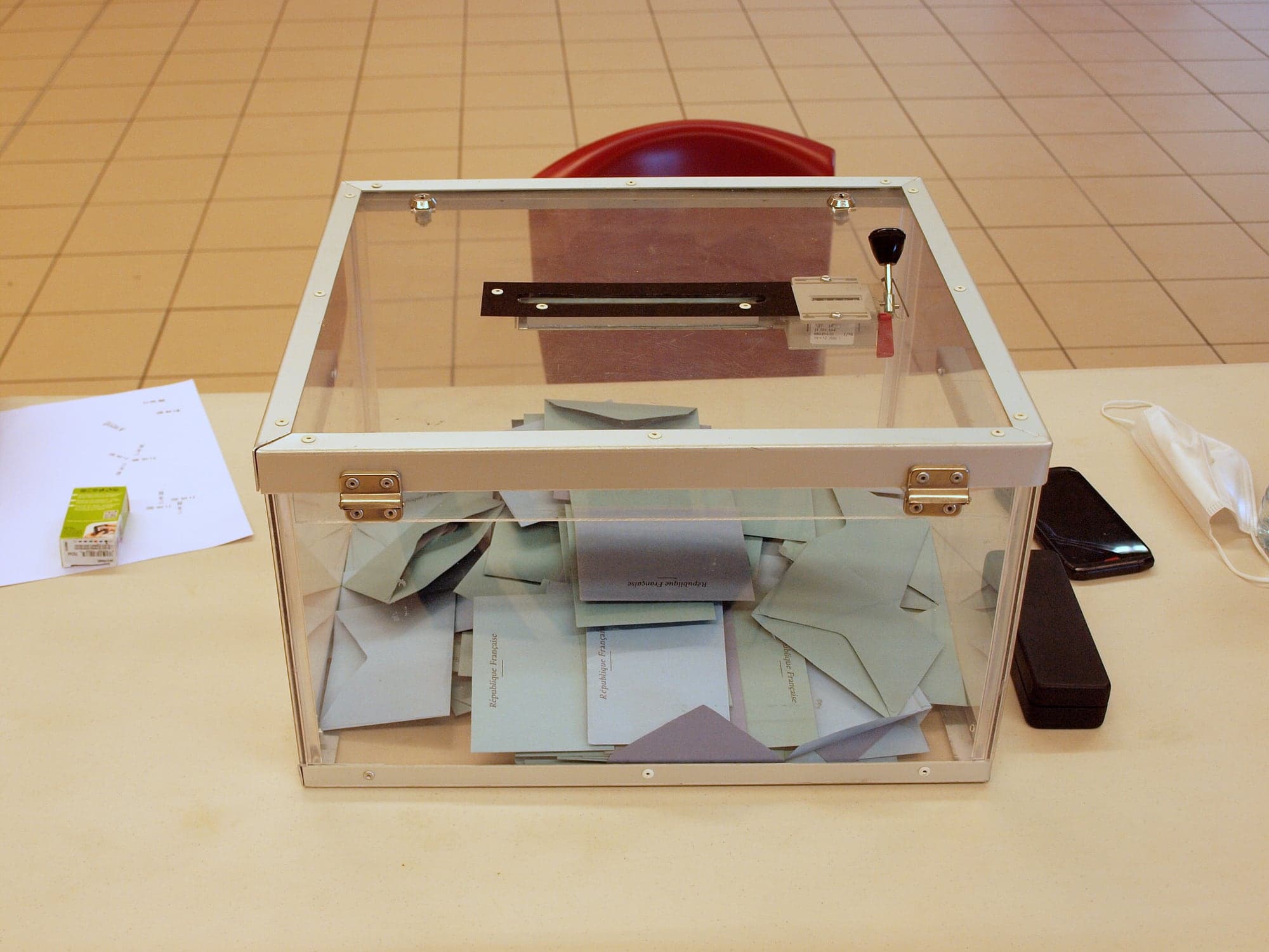Urne électorale transparente remplie d'enveloppes de vote « République française », posée sur une table dans un bureau de vote