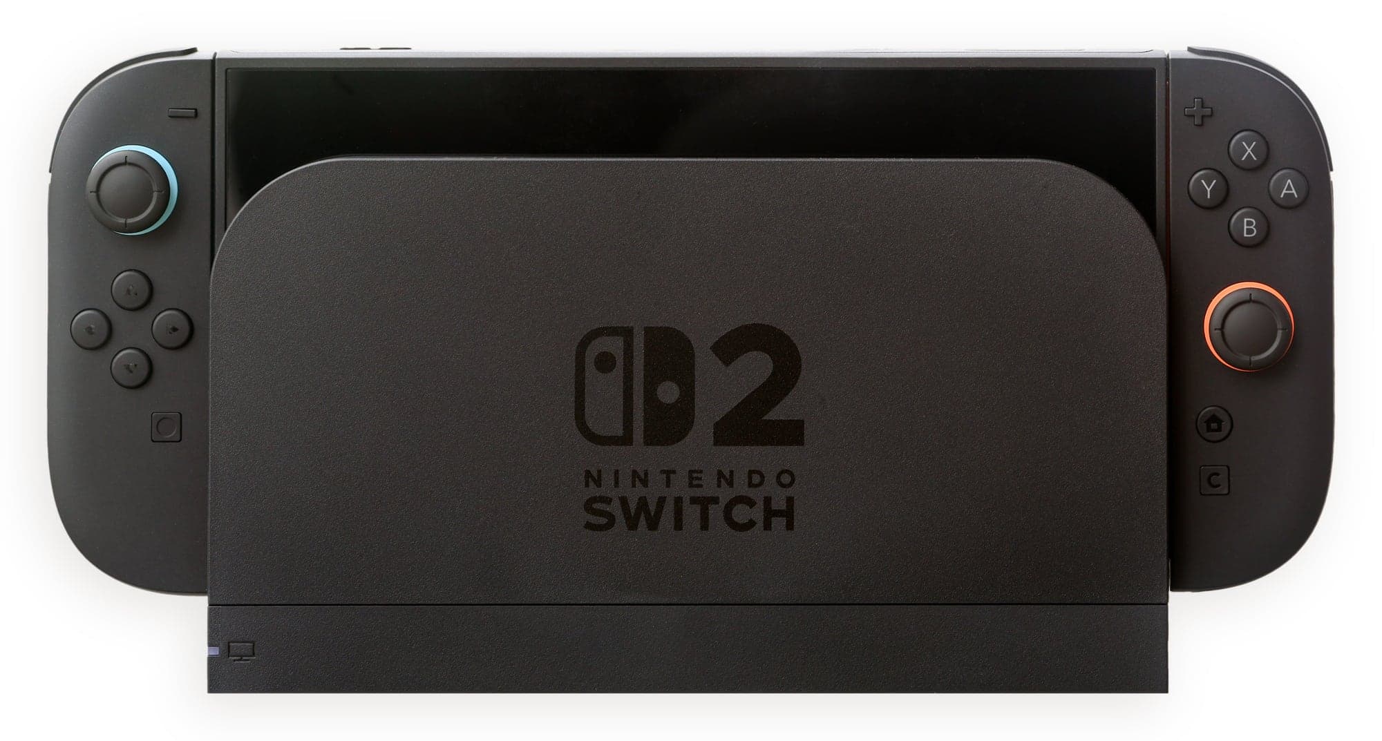 Une Nintendo Switch 2 posée dans sa station d'accueil noire marquée du logo Nintendo Switch 2, les deux Joy-Con 2 fixés de chaque côté de l'écran, avec leurs anneaux colorés autour des sticks (bleu à gauche, orange à droite), sur fond blanc.